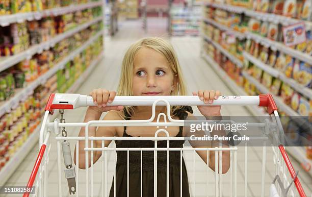 young girl pushing trolley in supermarket aisle - shopping trolley photos et images de collection