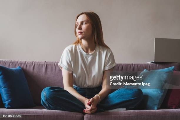 upset depressed young woman freelancer sitting on sofa with laptop looking out window - förödmjukelse bildbanksfoton och bilder
