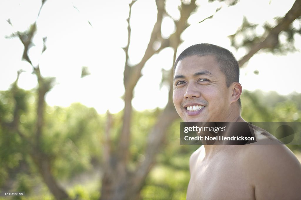 A male without his shirt off smiles at the beach