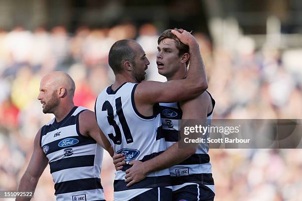 Tom Hawkins of the Cats is embraced by James Podsiadly and Paul Chapman after kicking a goal during the round 23 AFL match between the Geelong Cats...