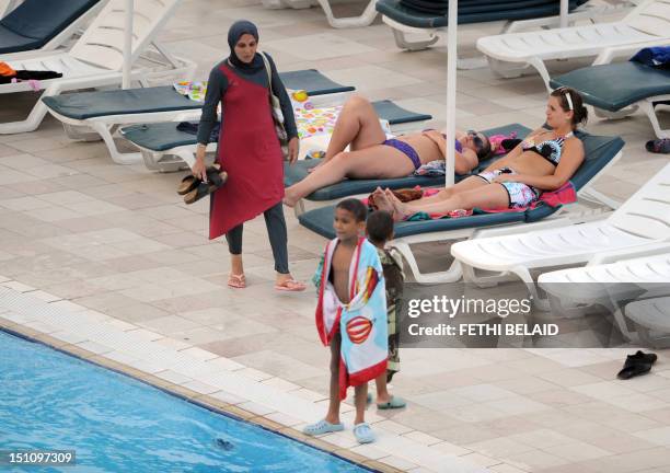 Woman wearing a swimming outfit or burkini that covers her body walks past women wearing bikinis at the pool of a hotel in the Tunisian coastal...