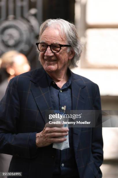 Paul Smith is seen wearing brown glasses, a dark blue suit jacket with big checked pattern in light brown and below it a dark blue buttoned shirt...