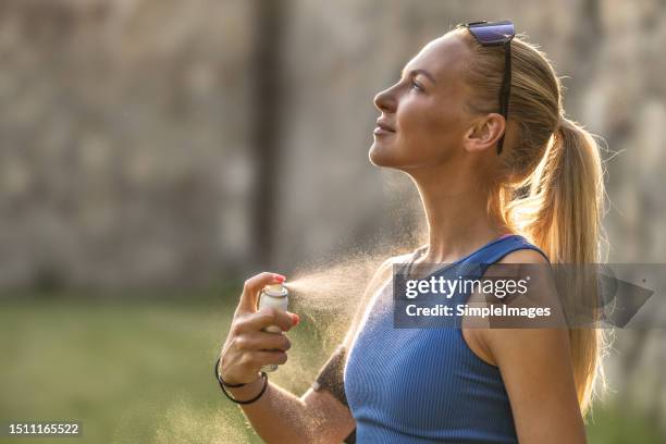 a young female athlete applies mosquito spray before jogging on a hot summer evening. - zanzara foto e immagini stock