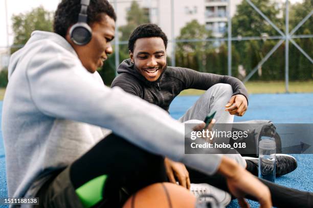 two friends hanging together on basketball court, using smart phone - streetball court stock pictures, royalty-free photos & images