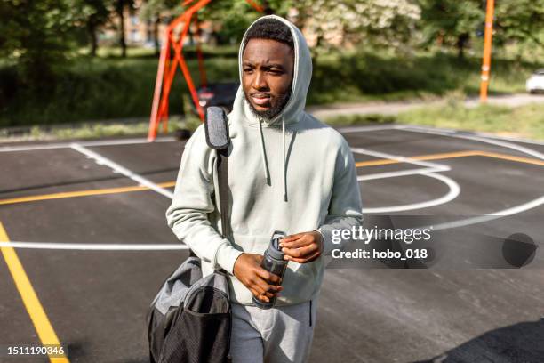 young man in a hoodie and gym bag at basketball court - basketball hoodie stock pictures, royalty-free photos & images