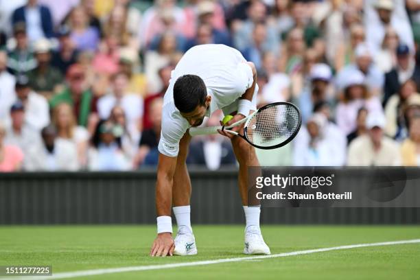 Novak Djokovic of Serbia wipes his hand on the grass against Pedro Cachin of Argentina in the Men's Singles first round match on day one of The...
