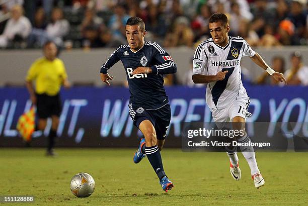 Russell Teibert of the Vancouver Whitecaps paces the ball on the attack under pressure from Hector Jimenez of the Los Angeles Galaxy in the first...