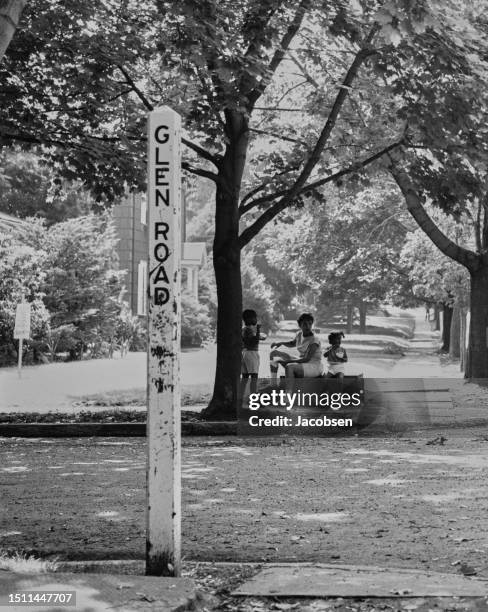 Mother and two children sitting in the shade of a tree on Glen Road, a residential street in Lakeview, Long Island, New York, circa 1965.