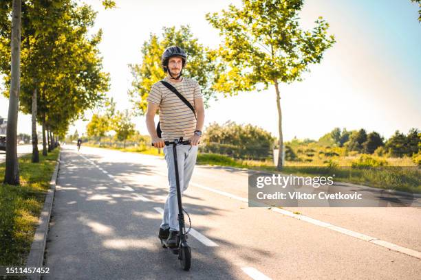 mann trägt schutzhelm beim fahren mit seinem e-scooter - roller fahren stock-fotos und bilder