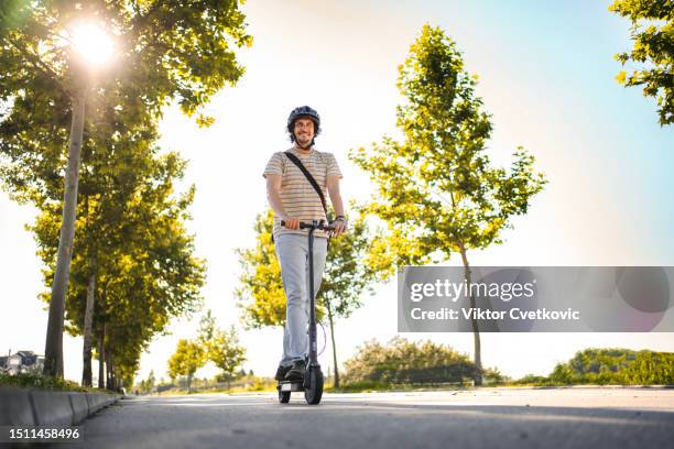 man wearing protective helmet while riding his e-scooter - trotinete imagens e fotografias de stock