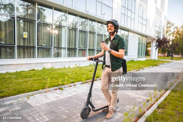 mann mit schutzhelm trinkt kaffee, während er auf seinem e-scooter zur arbeit geht - e scooter stock-fotos und bilder