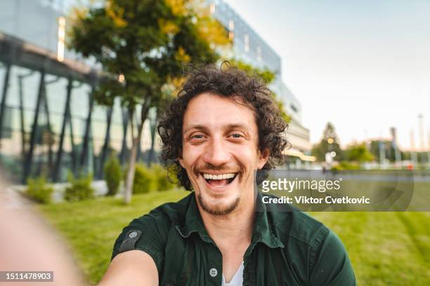portrait of a smiling man sitting on the grass in public park - mid adult man stock pictures, royalty-free photos & images