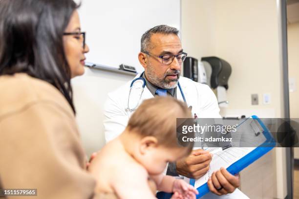 doctor speaks with a young woman holding her baby girl at the appointment reviewing the growth chart - growth chart stock pictures, royalty-free photos & images