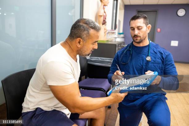 a male nurse showing a man how to fill his paperwork for the doctor appointment - er visit stock pictures, royalty-free photos & images