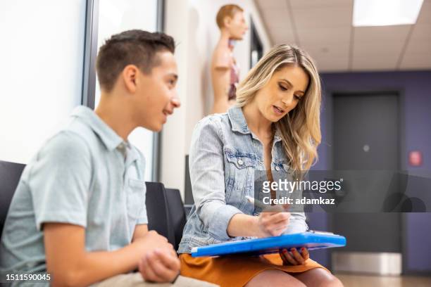 a woman fills out paperwork for the appointment at the doctors office - patient protection and affordable care act stock pictures, royalty-free photos & images