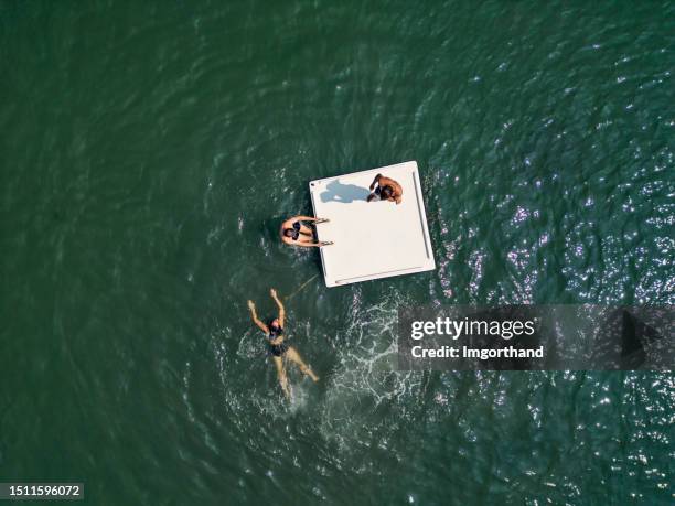 drone view of teenagers playing on a floating platform in the sea in liguria, italy - diving platform stock pictures, royalty-free photos & images
