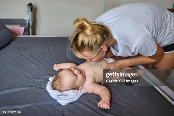 mother kissing belly of baby girl lying on bed in an apartment - baby girl laying on tummy stock pictures, royalty-free photos & images