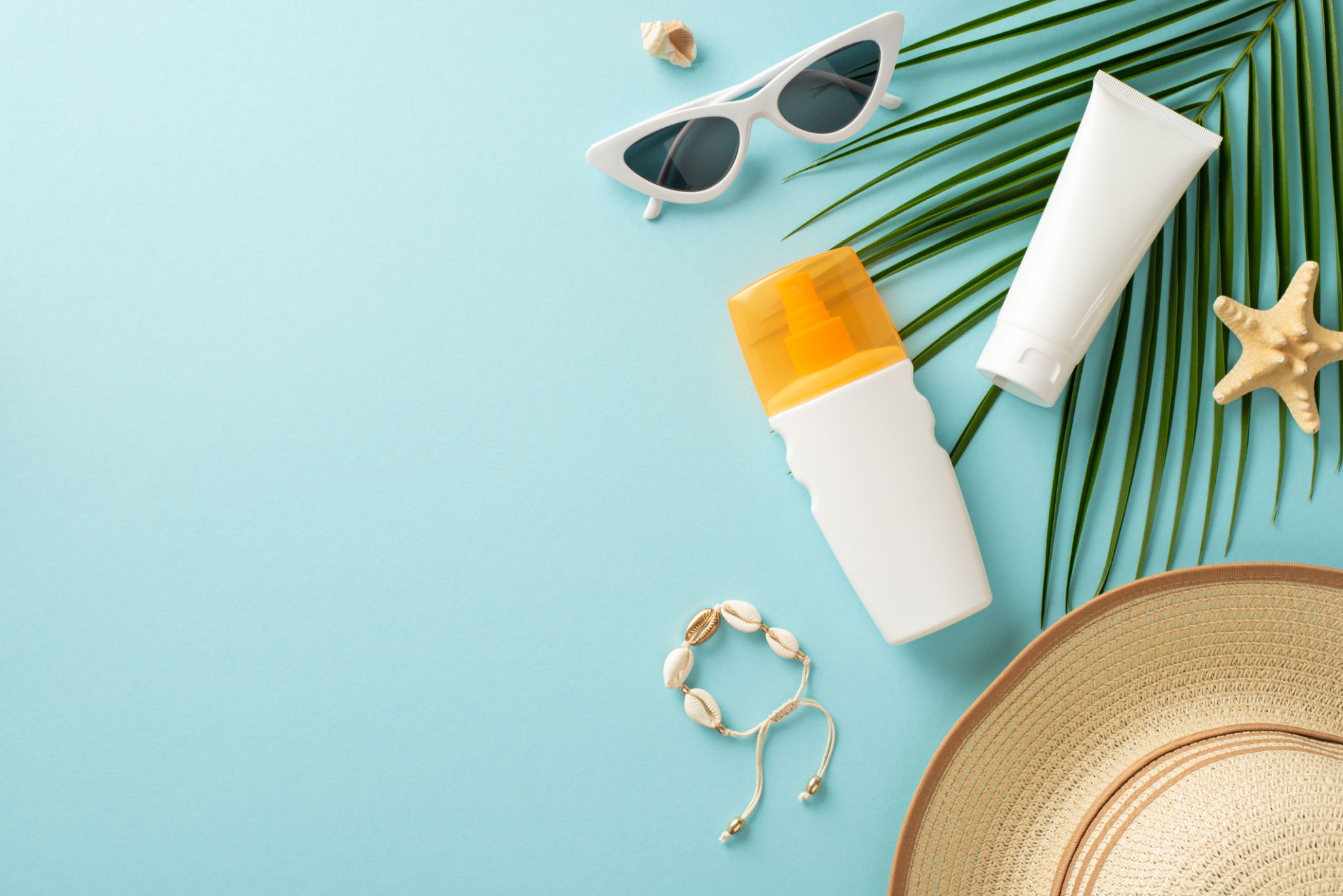 Embrace warmth of sun while protecting your skin. Top view of sunblock lotion and SPF cream tube without labels, eyeglasses, cap, shell bracelet, starfish, and a palm leaf on a pastel blue background Embrace warmth of sun while protecting your skin. Top view of sunblock lotion and SPF cream tube without labels, eyeglasses, cap, shell bracelet, starfish, and a palm leaf on a pastel blue background
