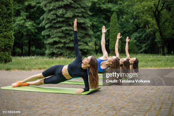 fit ladies dressed in comfy sports attire engaging in pilates exercises outdoors on overcast day - side plank pose stock pictures, royalty-free photos & images