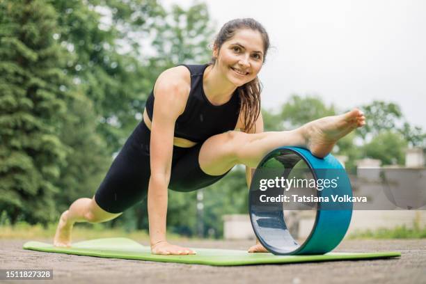 cheerful female pilates instructor doing whole-body stretching routine using pilates ring outside - adult gymnast feet stock-fotos und bilder