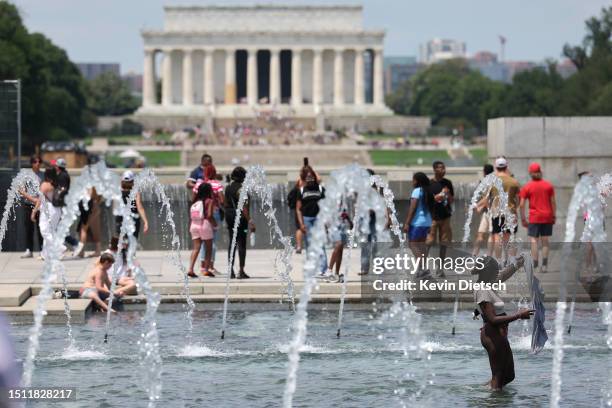 Visitors and tourists to the World War II Memorial seek relief from the hot weather in the memorial's fountain on July 03, 2023 in Washington, DC....