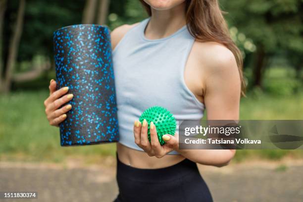 cropped image of unrecognizable female athlete in gray tank top holding yoga roll and massage ball standing in park - massage ball stock pictures, royalty-free photos & images