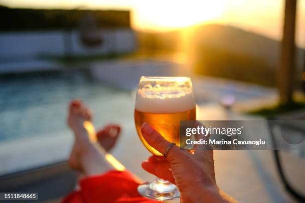 woman drinking beer with a pool view. personal perspective. - beer luxury stock-fotos und bilder