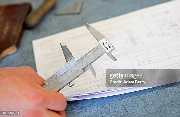 Trainee holds a caliper rule as he looks at technical plans for a project at a Siemens training center on September 3, 2012 in Berlin, Germany....