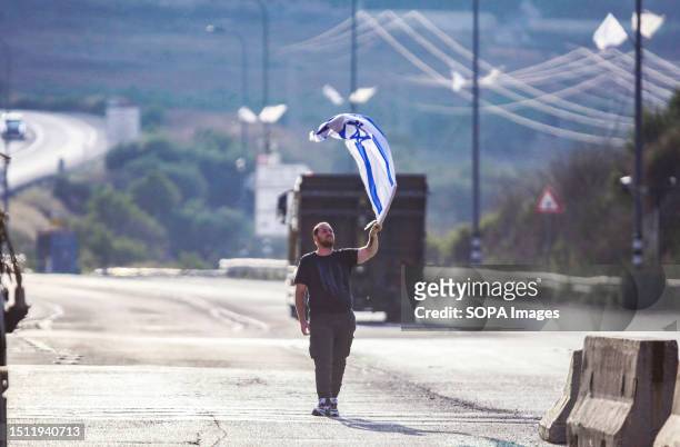 Jewish settler waves an Israeli flag in front of the Palestinians, after closing the road to the Palestinians, near the site of the shooting of an...