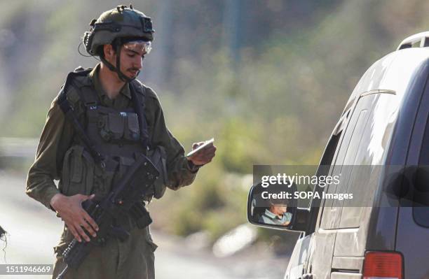 An Israeli soldier checks the phones of Palestinians who pass through an Israeli military checkpoint near the site of the shooting of an Israeli...