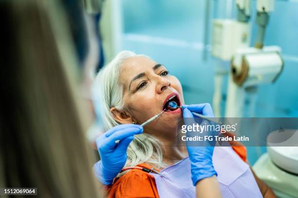 mature woman having teeth examined by a dentist at her office - inside human mouth stock pictures, royalty-free photos & images