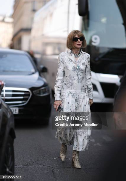 Anna Wintour is seen wearing black sunglasses in butterfly shape, a necklace with rose coloured and two with aqumarine coloured crystals/diamonds, a...