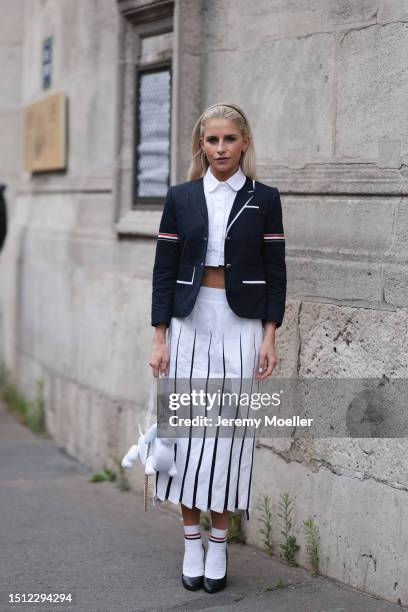 Caroline Daur is seen wearing a black hairband, golden earrings, an open dark blue blazer with white decorative seams from Thom Browne, below it a...