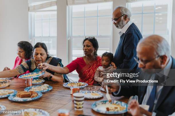 adoring grandparents cherish time with their grandchild at family reunion - indian family dinner table stock pictures, royalty-free photos & images