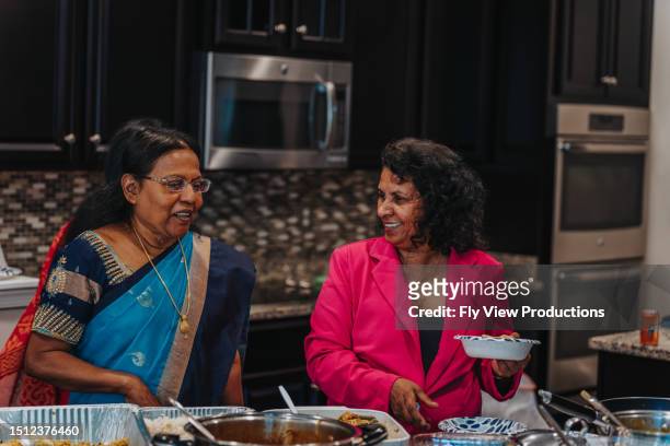 zwei indische frauen lächeln, als sie ein traditionelles essen servieren - oma feiert stock-fotos und bilder