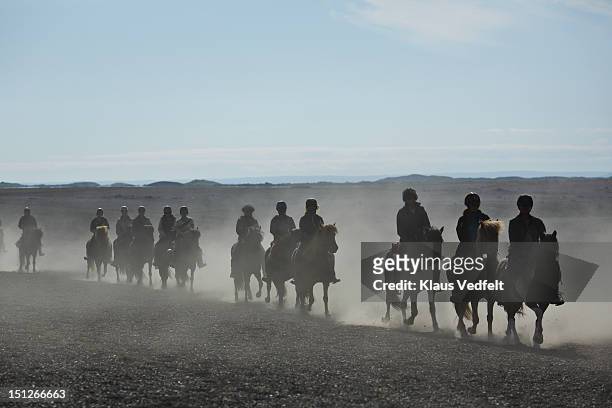Group of people on horses riding in dust cloud