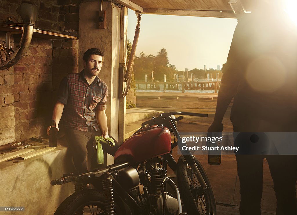 Males in garage with motorbike and beer