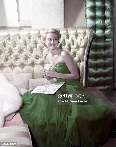 American actress Grace Kelly wearing a green dress for St Patrick's Day, 1954. She is reading a copy of MGM's Studio News.