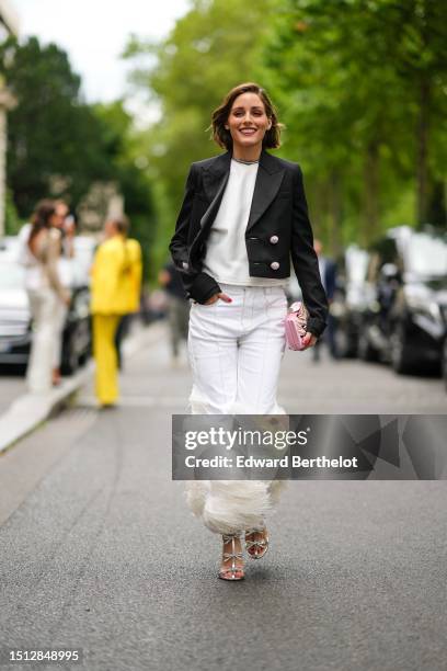 Olivia Palermo wears a silver and rhinestones necklace, a white t-shirt, a black with large rhinestones buttoned cropped jacket, white denim with...