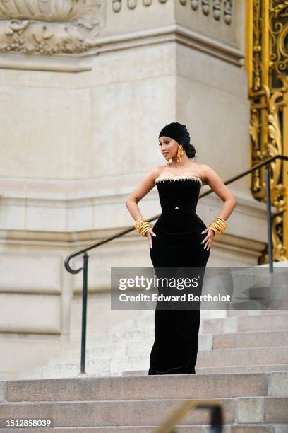 Cardi B wears a black velvet scarf as a hat from Schiaparelli, gold large ears and white pearls pendant earrings from Schiaparelli, a black velvet...