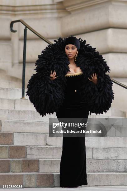 Cardi B wears a black velvet scarf as a hat from Schiaparelli, gold large ears and white pearls pendant earrings from Schiaparelli, a black velvet...