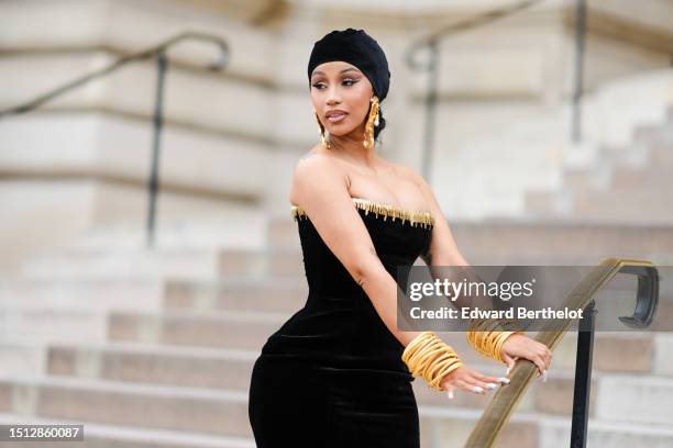 Cardi B wears a black velvet scarf as a hat from Schiaparelli, gold large ears and white pearls pendant earrings from Schiaparelli, a black velvet...
