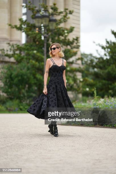 Chiara Ferragni wears black sunglasses from Ray Ban, diamonds micro earrings, gold large pendant earrings from Schiaparelli, a black silk with...