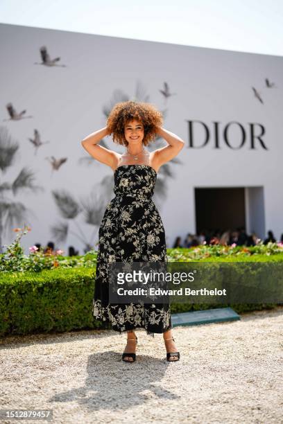 Lena Mahfouf wears a silver and diamonds flower pendant necklace, a black with embroidered gold birds pattern shoulder-off / midi dress from Dior,...