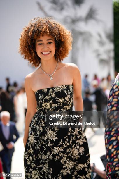 Lena Mahfouf wears a silver and diamonds flower pendant necklace, a black with embroidered gold birds pattern shoulder-off / midi dress from Dior,...