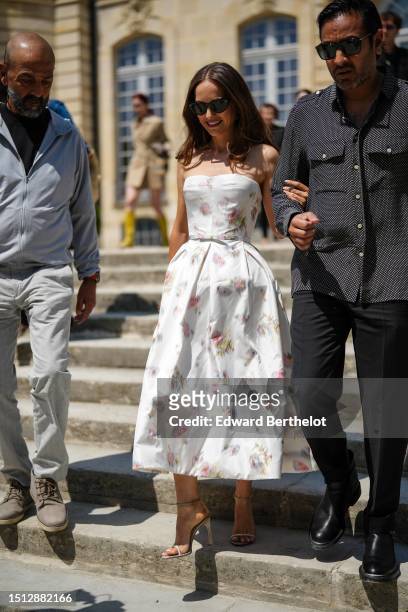Natalie Portman wears black sunglasses, a white with pale painted pattern shoulder-off / silk puffy midi dress, a white matte leather leather...