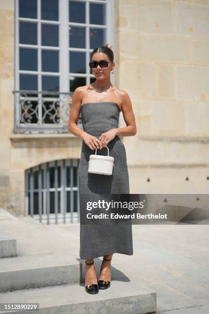 Camila Coelho wears black squared sunglasses from Dior, gold earrings, a gray shoulder-off / tube midi dress, a white matte leather zipper Vanity...