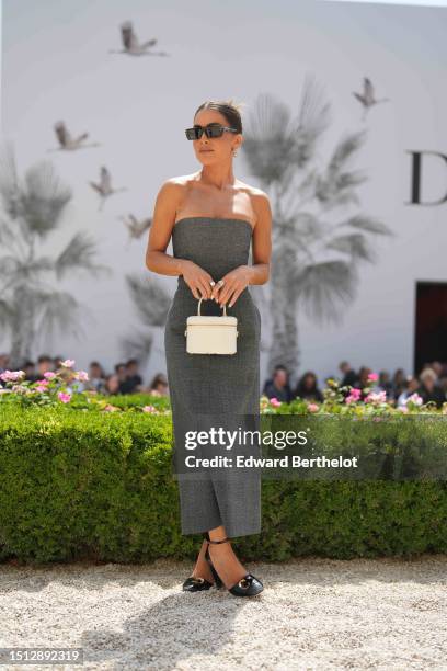 Camila Coelho wears black squared sunglasses from Dior, gold earrings, a gray shoulder-off / tube midi dress, a white matte leather zipper Vanity...