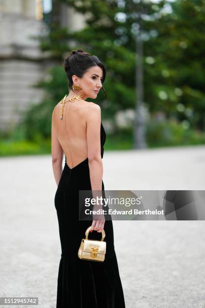 Alexandra Pereira wears gold large lips pendant earrings from Schiaparelli, a black velvet with gold metallic neck strap / long mermaid dress from...