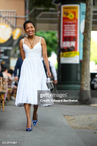 Tamu McPherson wears white large pearl / long pendant earrings, a black / yellow / red / green pearls with a gold T pendant necklace, a white V-neck...